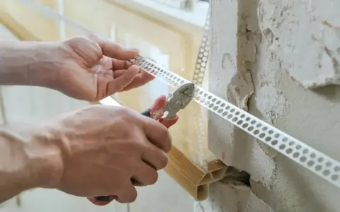 Ręce przycinają narożnikową listwę perforowaną, która posłuży jako wzmocnienie pod gips do narożników.