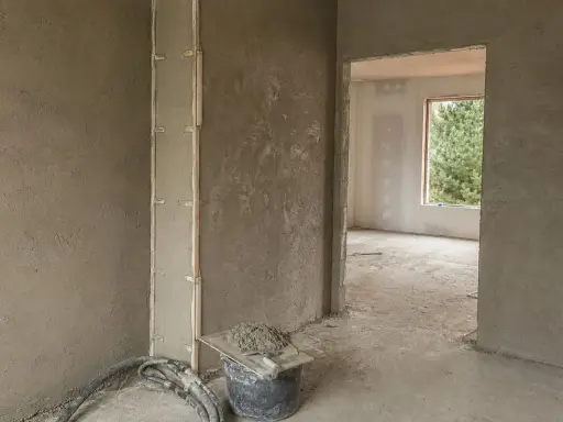 Ściany pokryte tynkami gipsowymi w nieogrzewanym domu. Widać wiadro z zaprawą i narzędzia.