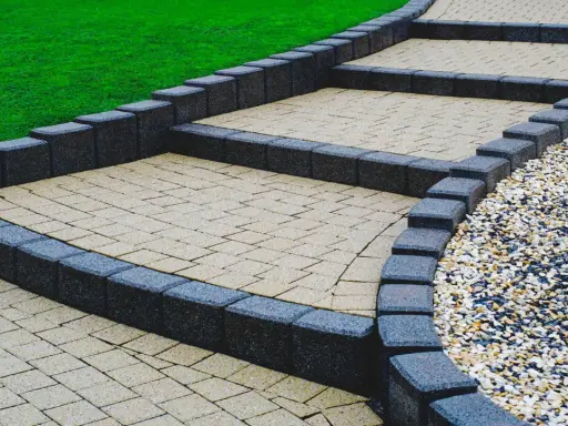 Schody z palisad prowadzą przez zadbany ogród. Jasne stopnie z kostki brukowej kontrastują z ciemnymi obrzeżami.