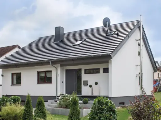 Nowoczesny dom z białymi ścianami i szarym dachem o nachyleniu 45 stopni. Na dachu komin i antena satelitarna.