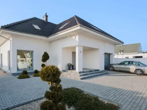 Nowoczesny dom z podjazdem wyłożonym starą kostką brukową, na którym stoi srebrny samochód.