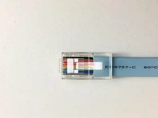 Przezroczysta wtyczka RJ45 z kolorowymi żyłkami kabla sieciowego, przypominająca budową kabel FTP a UTP.
