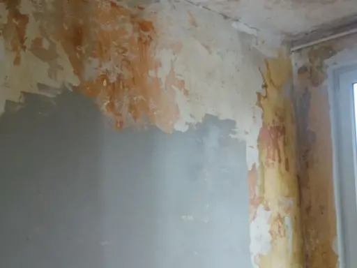 Ściana z odpadającą farbą i tynkiem, przygotowywana do remontu. Widać fragmenty szarej gładzi, które pomogą jak naprawić kratery w gładzi gipsowej.