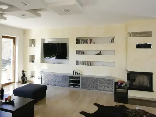 Nowoczesna zabudowa pod telewizor z regipsu z wnękami na książki i dekoracje.