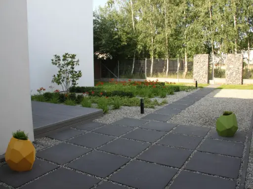 Nowoczesny ogród z kamieniami zamiast trawnika, z geometrycznymi donicami i ścieżką z płyt.