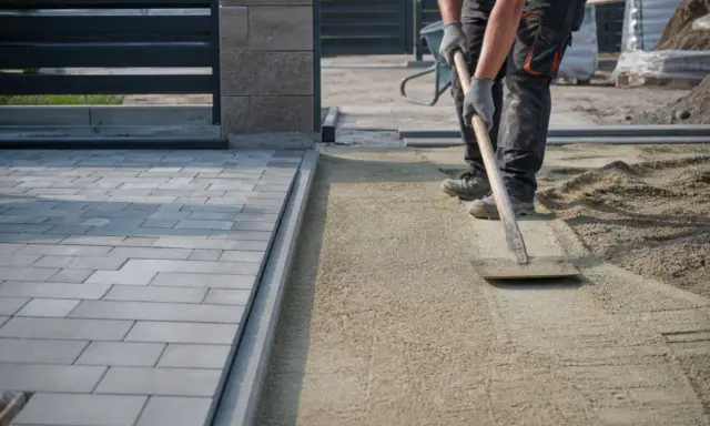 Pracownik wyrównuje piasek, przygotowując podbudowę pod chodnik.