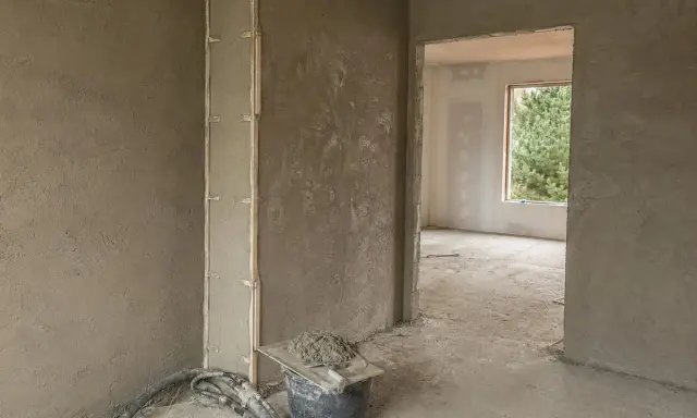 Ściany pokryte tynkami gipsowymi w nieogrzewanym domu. Widać wiadro z zaprawą i narzędzia.
