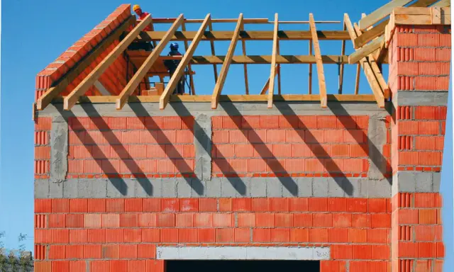Budowa domu: drewniana konstrukcja dachu i ścianka kolankowa z profili na tle błękitnego nieba.