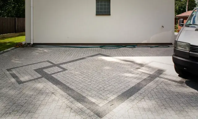 Nowoczesne układanie kostki na grysie z geometrycznym wzorem. Wjazd do domu z szarej kostki.