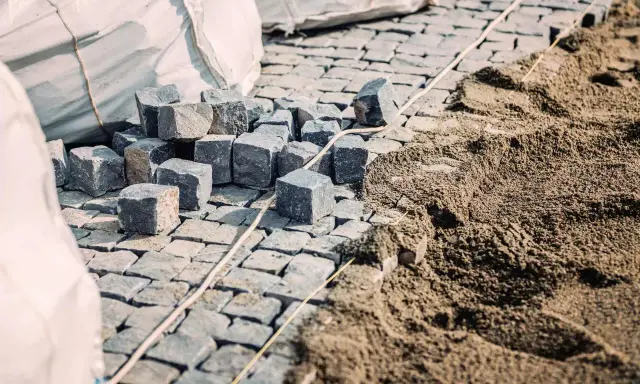 Kupa kostki brukowej czeka na ułożenie. Widać sporo piasku pod kostkę, gotowego do pracy.