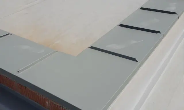 Szary parapet dachowy, element montażu rynien plastikowych, zabezpiecza mur przed wilgocią.