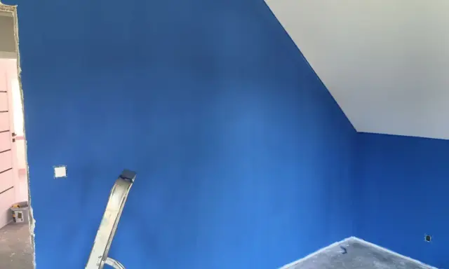 Niebieskie ściany z widocznymi smugami po malowaniu. Drabina stoi przy ścianie, a sufit jest biały.