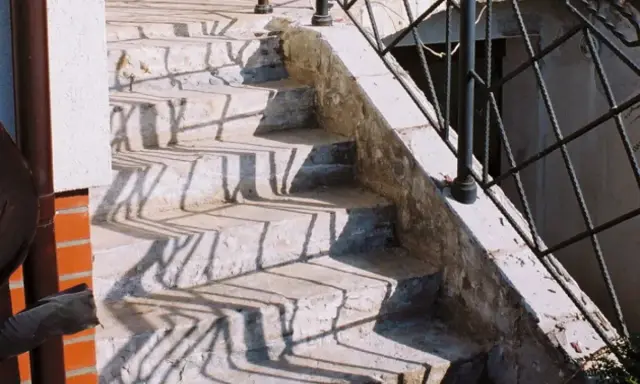 Kamienne stopnie schodów zewnętrznych, z widocznymi cieniami balustrady. Jaki beton na schody zewnętrzne? Ten wygląda na solidny.