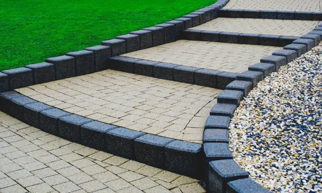 Schody z palisad prowadzą przez zadbany ogród. Jasne stopnie z kostki brukowej kontrastują z ciemnymi obrzeżami.