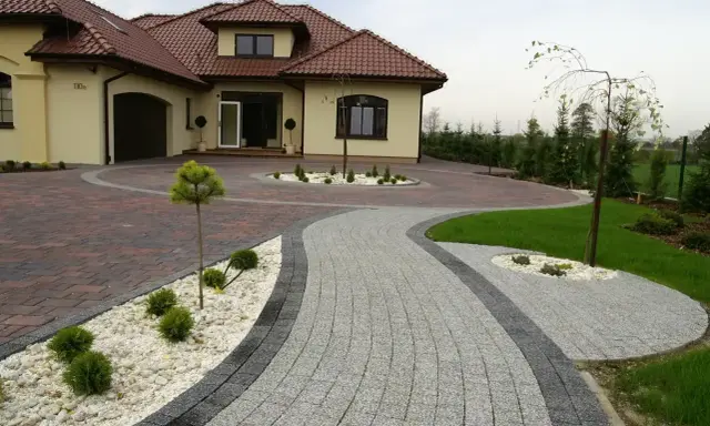 Eleganckie układanie kostki brukowej wokół nowoczesnego domu. Dwa rodzaje kostki tworzą efektowną ścieżkę i podjazd.