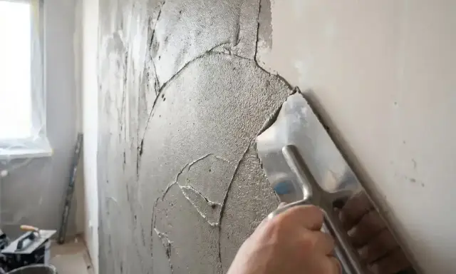 Ręka zacierająca świeżą masę naprawczą do tynku cementowo-wapiennego na ścianie.