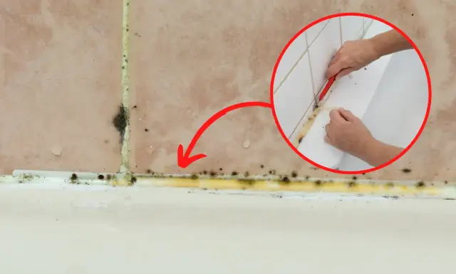 Pokazano, jak usunąć stary silikon z pleśnią. Dłoń z nożykiem usuwa żółty, zapleśniały silikon z fugi przy wannie.