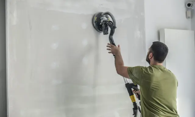 Mężczyzna szlifuje tynk cementowo-wapienny przed malowaniem. Gładka ściana czeka na farbę.