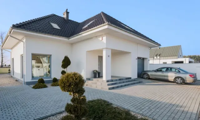 Nowoczesny dom z podjazdem wyłożonym starą kostką brukową, na którym stoi srebrny samochód.