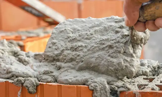 Robotnik nakłada zaprawę kielnią na cegły. Obraz pokazuje, ile tynku na m2 potrzeba do budowy.