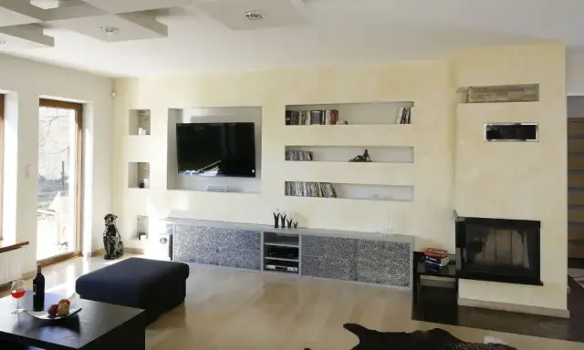Nowoczesna zabudowa pod telewizor z regipsu z wnękami na książki i dekoracje.
