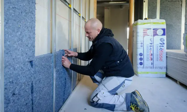 Budowlaniec montuje izolację na stelażu, przygotowując ścianę pod karton gips.