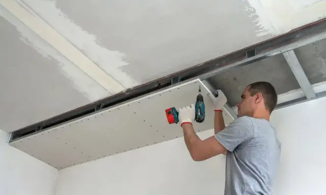 Mężczyzna przykręca płytę kartonowo-gipsową do stelaża sufitowego. Do cięcia karton gips używa się specjalnych narzędzi.