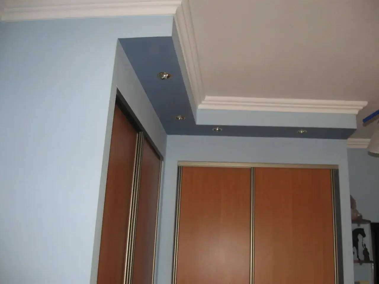 Elegancka zabudowa rur pod sufitem z wbudowanymi punktami świetlnymi, nad szafami wnękowymi.