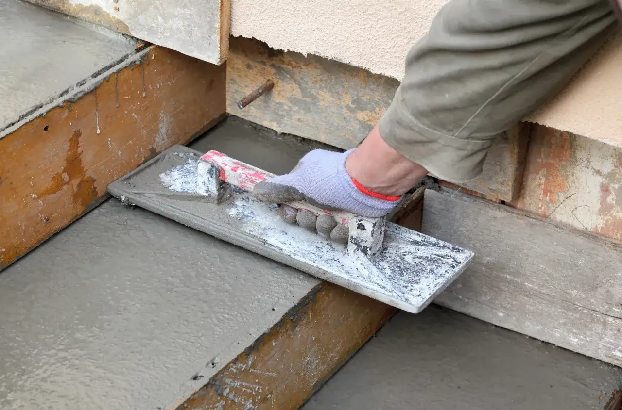 Ręka w rękawiczce wygładza świeży beton na schodach zewnętrznych. Odpowiedni jaki beton na schody zewnętrzne zapewnia trwałość.
