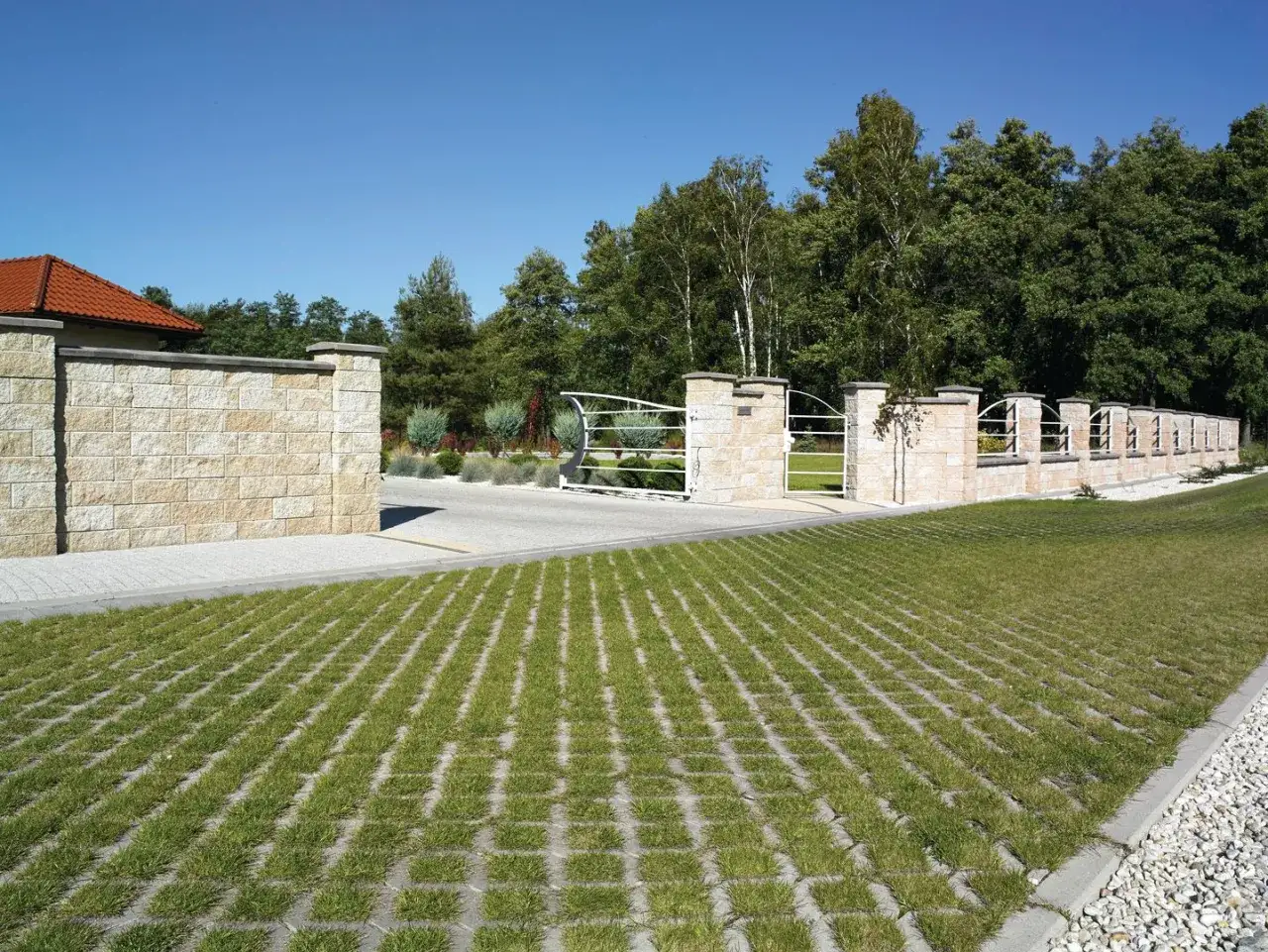 Nowoczesne podw&oacute;rko utwardzone ekologiczną kratką trawnikową, kamiennym murem i elegancką bramą.