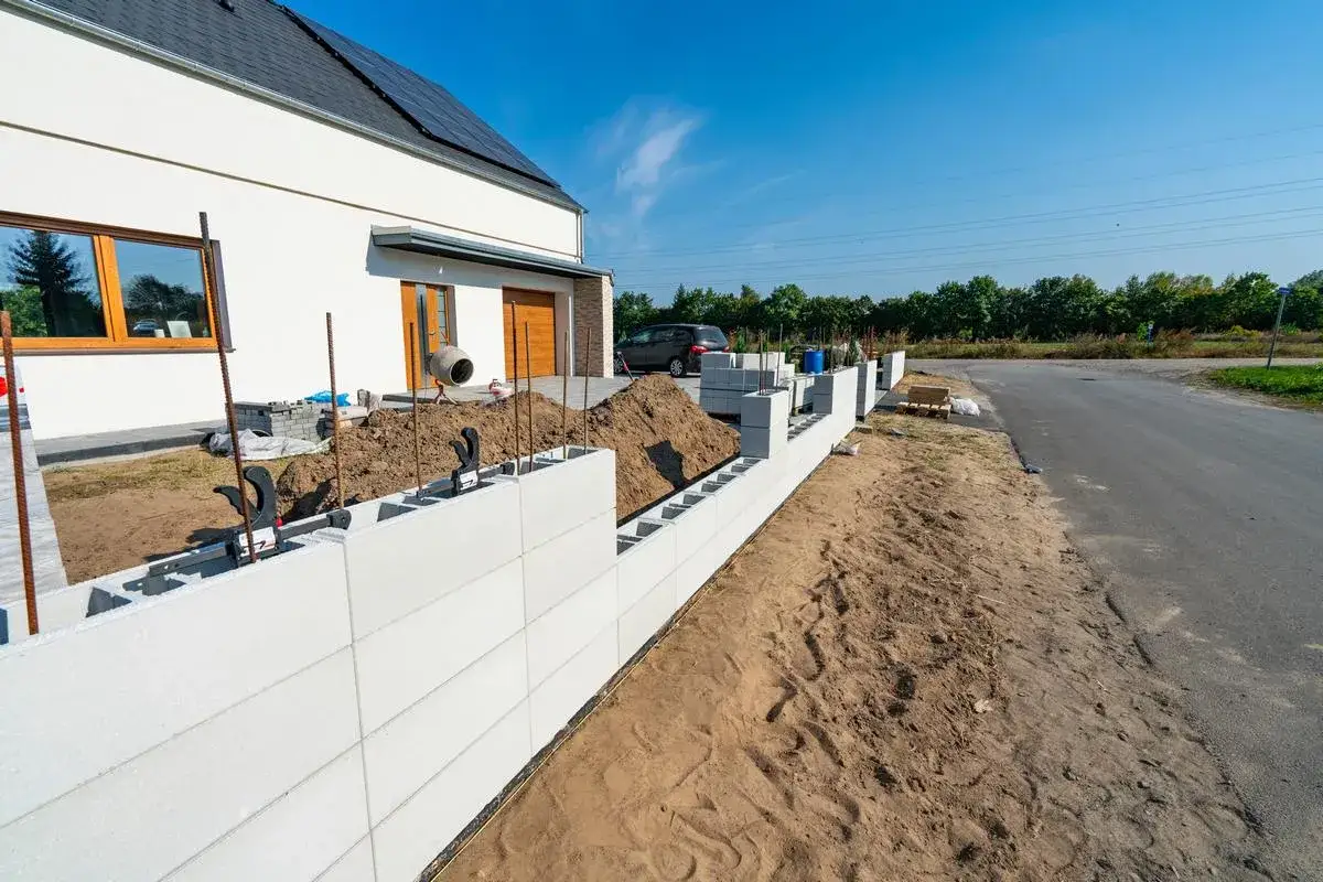 Budowa ogrodzenia z bloczk&oacute;w fundamentowych przy nowym domu. Widać zbrojenie i stosy bloczk&oacute;w.