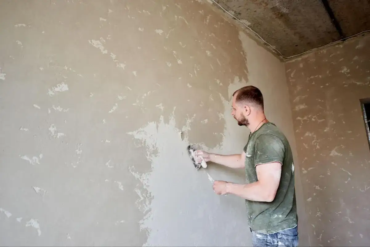 Mężczyzna szlifuje tynk cementowo-wapienny przed malowaniem. Prace wykończeniowe w nowym domu.