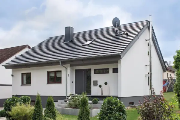 Nowoczesny dom z białymi ścianami i szarym dachem o nachyleniu 45 stopni. Na dachu komin i antena satelitarna.