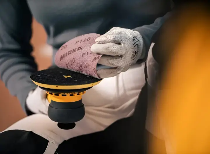 Ręka w rękawicy zakłada siatkę do szlifowania gipsu na talerz szlifierki.